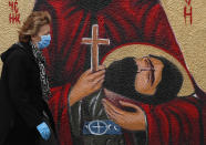 A woman wearing a protective face mask passes by graffiti depicting a Christian Orthodox icon in Belgrade, Serbia, Wednesday, May 27, 2020. (AP Photo/Darko Vojinovic)