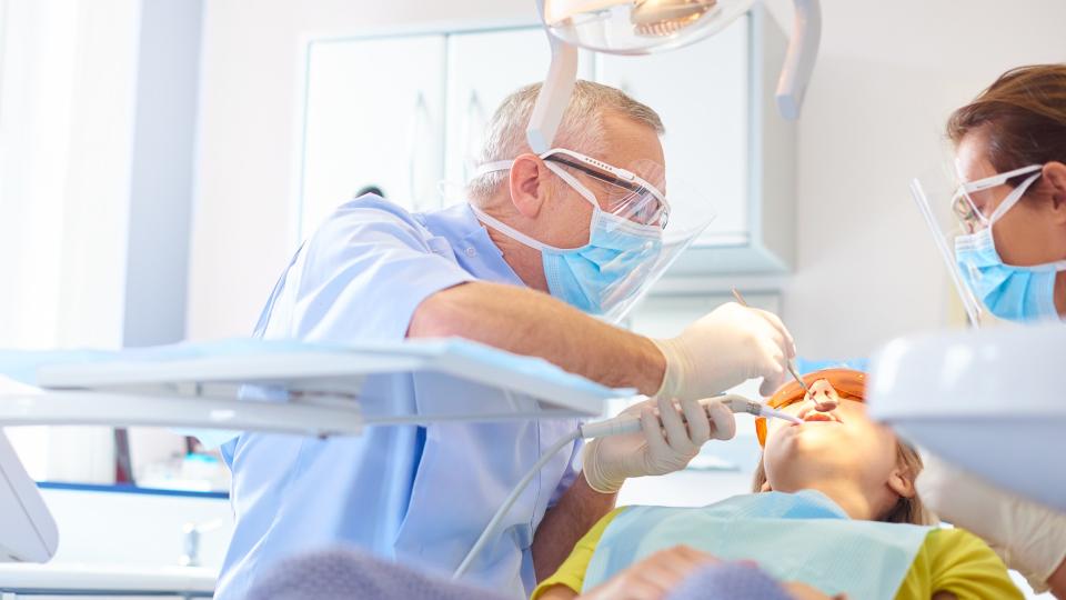 A senior dentist performing a dental procedure on young woman.