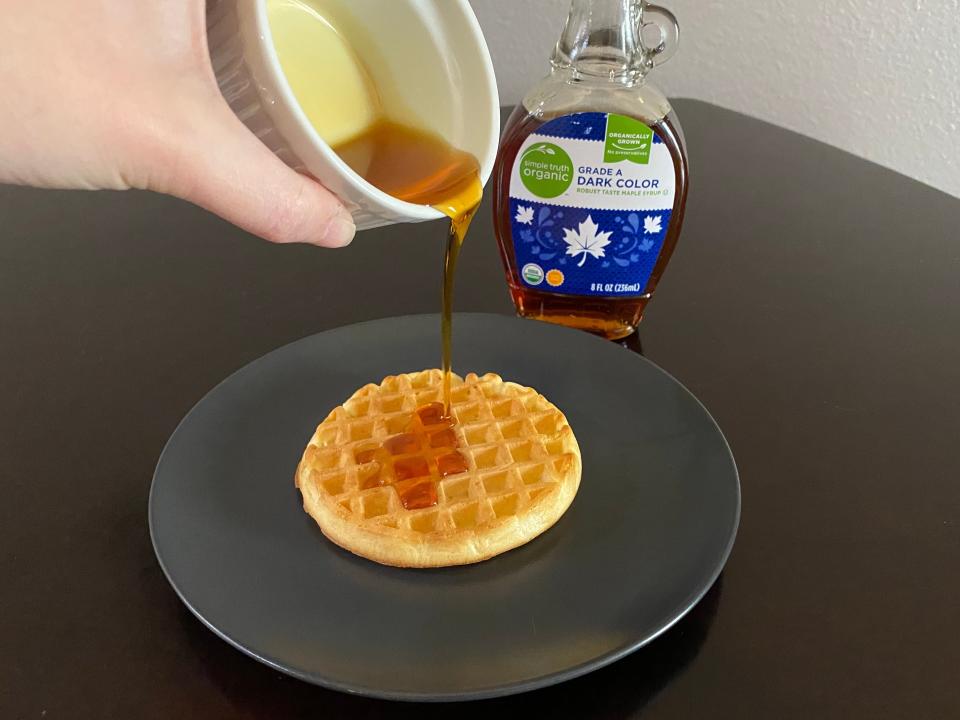 hand pouring ramekin of kroger maple syrup over a toaster waffle