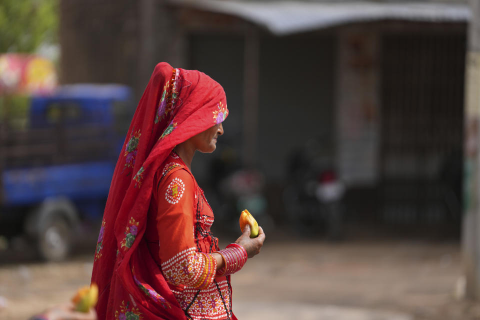 A nomadic woman walks eating a fruit on a hot summer afternoon in Lalitpur district in northern Uttar Pradesh state, India, Sunday, June 18, 2023. Swaths of two of India's most populous states are under a grip of sever heat leaving dozens of people dead in several days as authorities issue a warning to residents over 60 and others with ailments to stay indoors during the daytime. (AP Photo/Rajesh Kumar Singh)