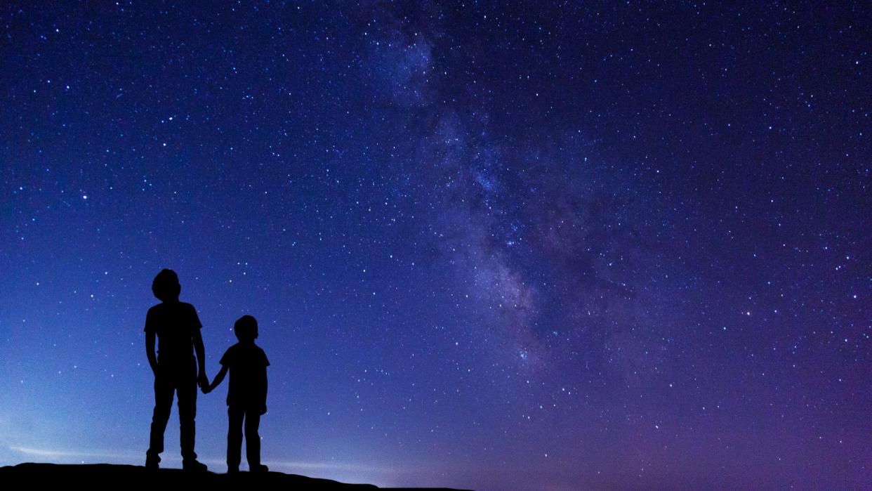  Silhouettes of two children looking up at the night sky. 