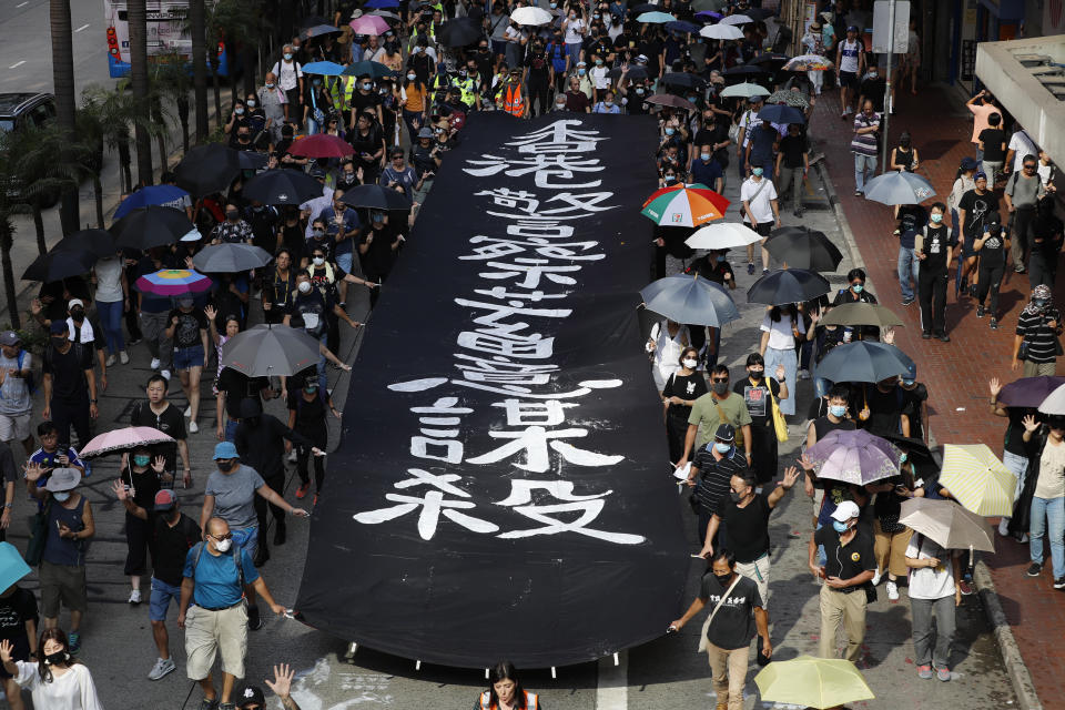 Masked protesters walk next to a banner that reads "Hong Kong police deliberately murder" in Hong Kong on Saturday, Oct. 5, 2019. All subway and trains services are closed in Hong Kong after another night of rampaging violence that a new ban on face masks failed to quell. (AP Photo/Vincent Thian)