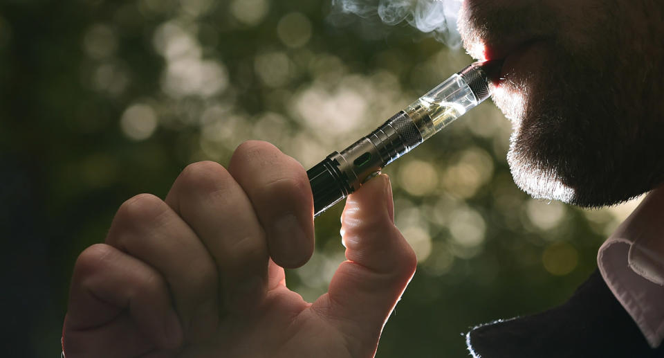 Pictured is a man vaping or smoking an e-cigarette. 