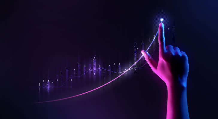 Hand pointing upward next to upward trend stock chart in purple and blackish blue lighting, symbolizes growth stocks