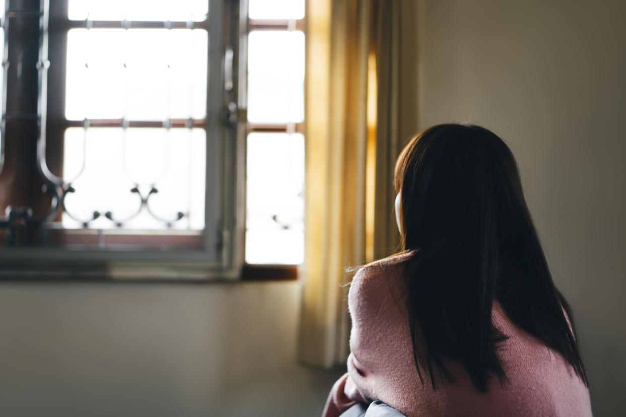 Lockdown city and people stay at home concept. Rear view of young asian teenager woman lonely and tired sit near window. Quarantine form virus corona pandemic.