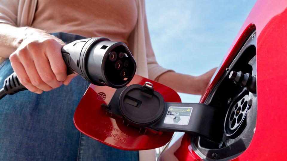  Horizontal cropped view of female hand plugging the cord into red electric car to charge battery at home