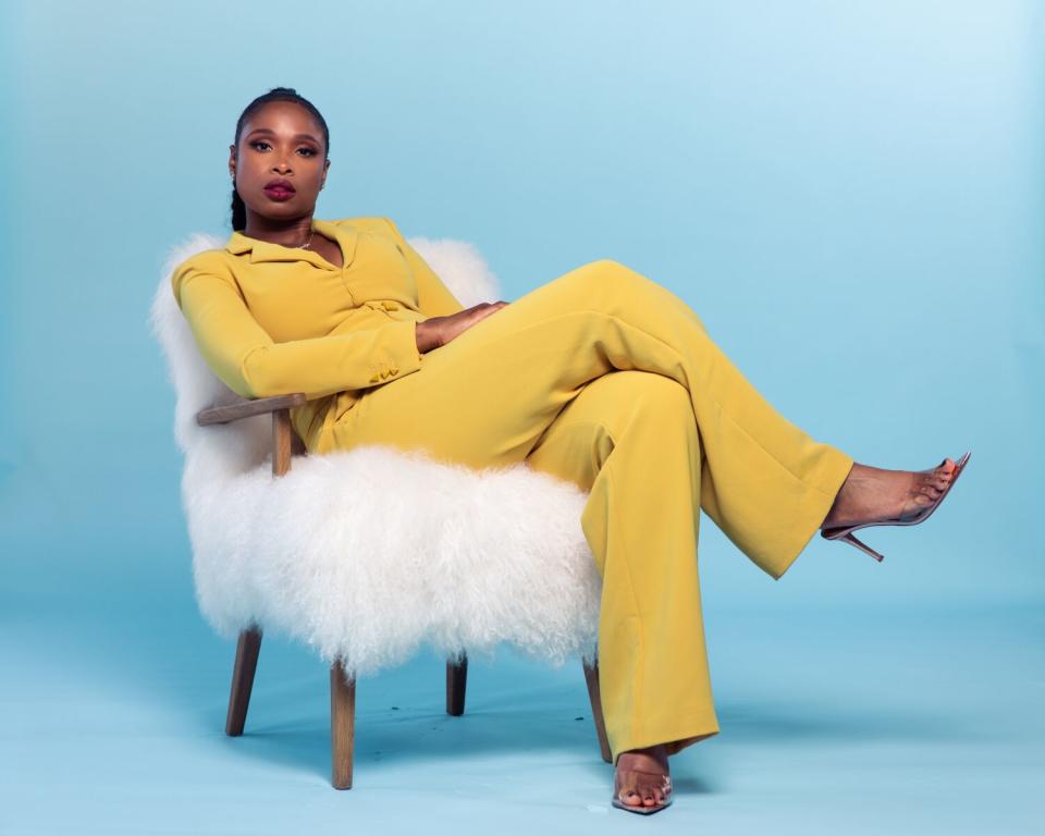 Jennifer Hudson in a yellow pantsuit sitting on a fluffy white chair
