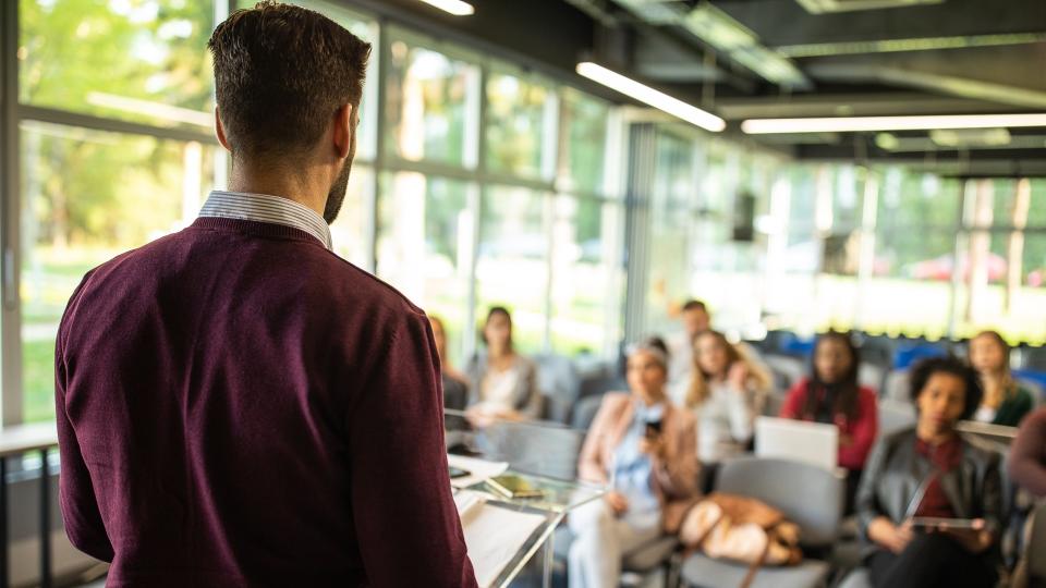 Unrecognizable businessman  giving his team a business presentation in a board room, making a speech, colleagues listening, rear view.