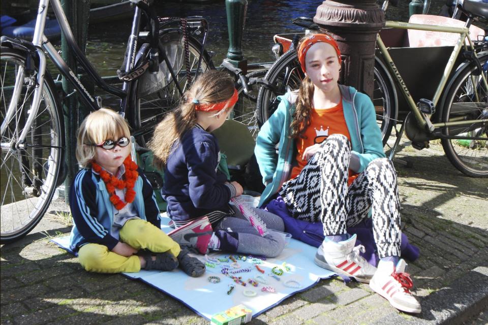 Children wait for clients to buy their goods at the annual free market during festivities marking King's Day in Amsterdam, Netherlands, Saturday, April 26, 2014. The Dutch celebrate the first ever King's Day, a national holiday held in honor of the newly installed monarch, King Willem Alexander. King's Day replaces the traditional Queen's Day. (AP Photo/Margriet Faber)