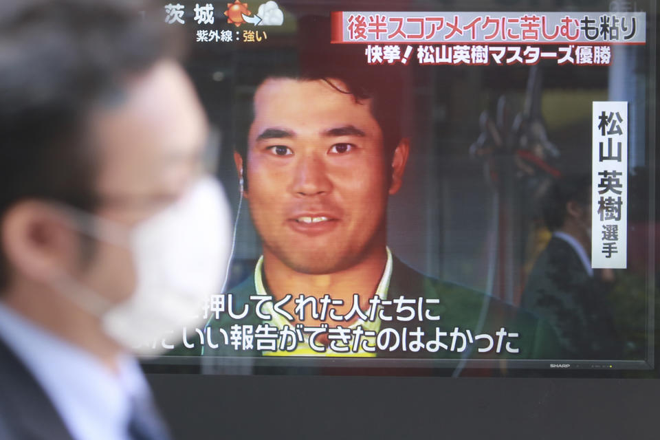 People walk past the tv screen showing the image of Japanese golfer Hideki Matsuyama in a news channel in Tokyo, Monday, April 12, 2021. From Japan's prime minister on down, the country celebrated Matsuyama's victory in the Masters — the first Japanese to win at Augusta National and wear the famous green jacket.(AP Photo/Koji Sasahara)