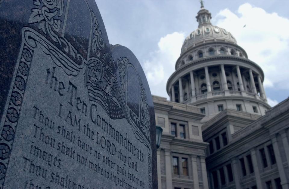 The dome of a white, ornate building rises in the background, and a gray monument with writing sits in the foreground.