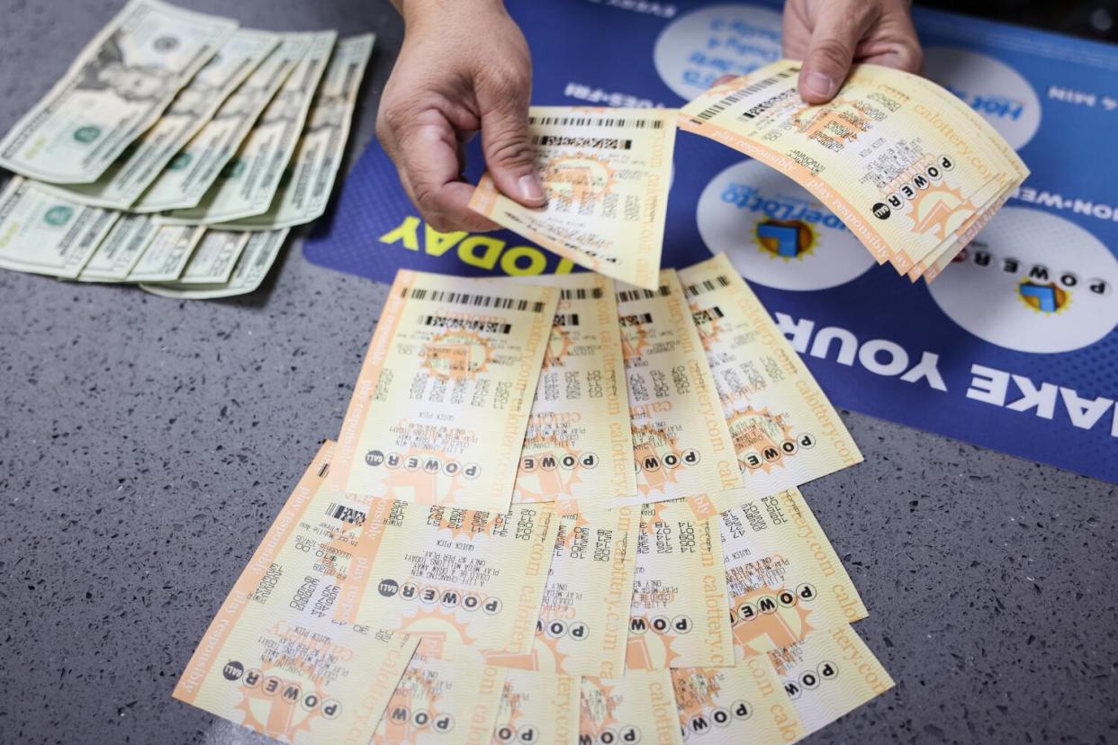 A cashier lays out several Powerball lottery tickets on the counter next to several $20 bills