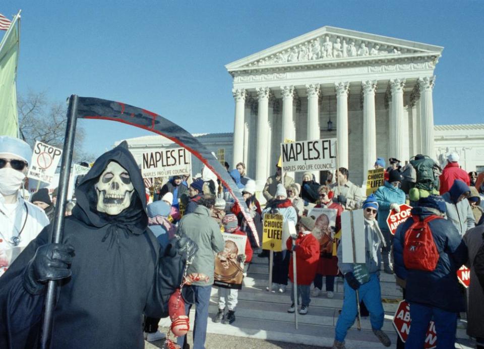 A person is dressed as the grim reaper while others hold signs saying 'Naples pro-life council'