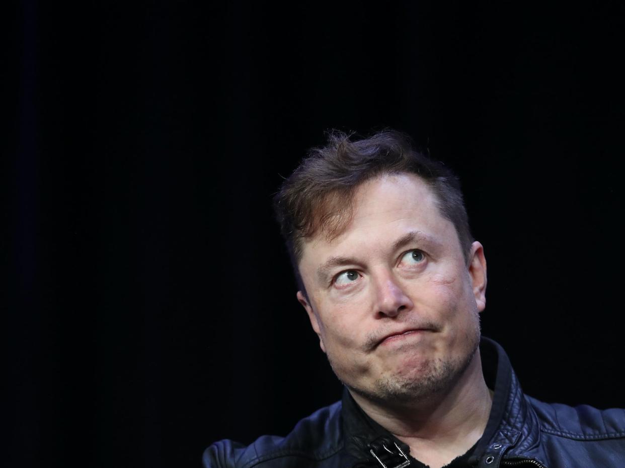 Elon Musk grimaces while looking off to side against black backdrop