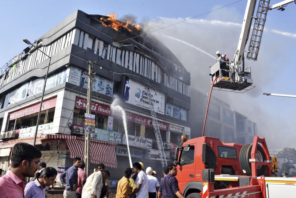 Firefighters work to douse flames on a building in Surat, in the western Indian state of Gujarat, Friday, May 24, 2019. At least 17 teenage students were killed in a fire that broke out Friday in a four-story building, police said. Television images showed some students jumping from the building to escape the blaze with a thick smoke billowing from the building. (AP Photo/Sarju Parekh)