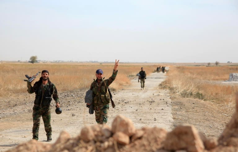Syrian regime soldiers gesture as they walk down a road in an area around Kweyris military airport, in the eastern Aleppo province on October 18, 2015