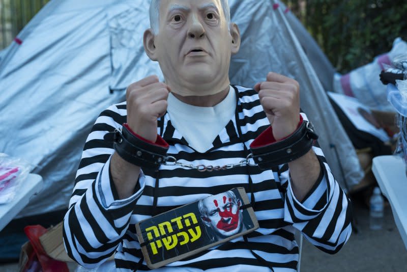 Wearing a sign that reads "impeachment now," a protestor wears a mask of Israeli Prime Minister Benjamin Netanyahu outside a tent during mass protests opposite the government offices of Prime Minister Benjamin Netanyahu and the Knesset in Jerusalem on Tuesday. Photo by Jim Hollander/UPI