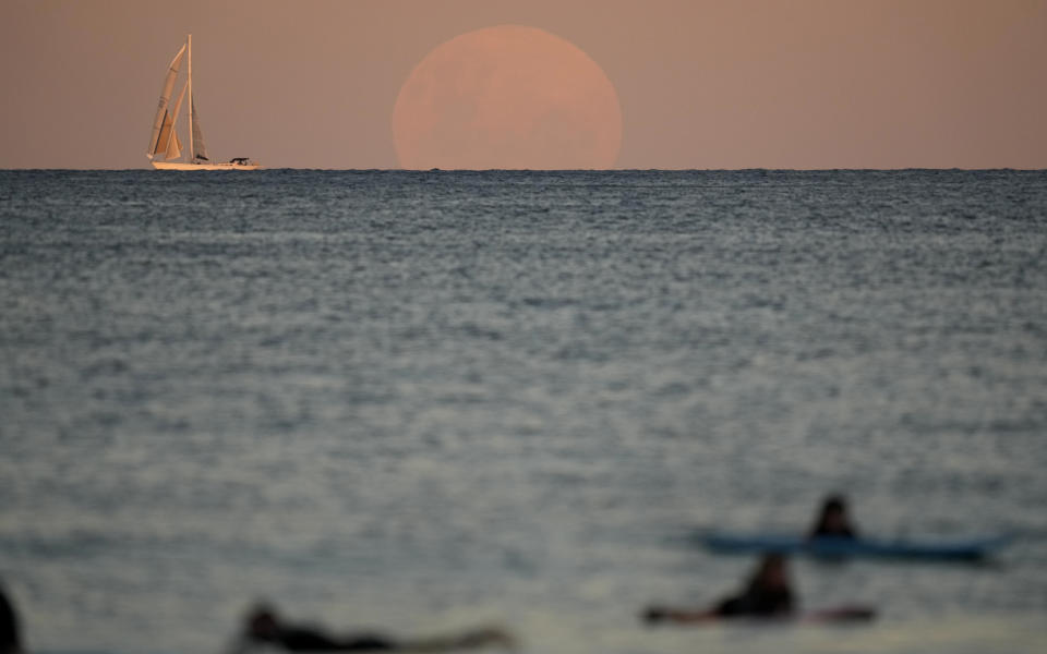 A yacht sails past as the moon rises in Sydney Wednesday, May 26, 2021. A total lunar eclipse, also known as a Super Blood Moon will take place later tonight as the moon appears slightly reddish-orange in color. (AP Photo/Mark Baker)
