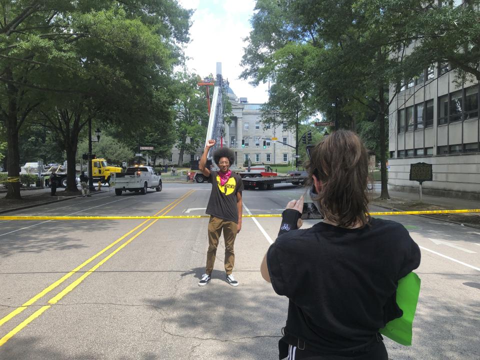 A man raises his fist in the Black Power salute as workers behind him disassemble the remains of a large Confederate memorial on the grounds of the Old Capitol in Raleigh, N.C., on Sunday, June 21, 2020. After protesters pulled down two smaller statues on the same monument Friday, North Carolina Gov. Roy Cooper ordered the removal of several other monuments to the Confederacy, citing public safety concerns. (AP Photo/Allen G. Breed)