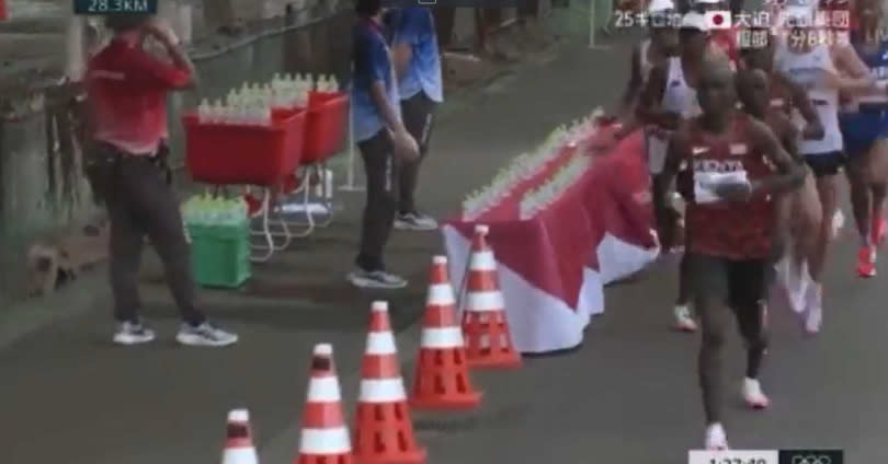 安姆杜尼在馬拉松比賽時，伸手推倒桌上整排水瓶。（圖／翻攝自@rinzinbizin推特）