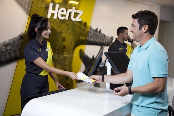 Hertz counter with employee handing rental agreement to customer.