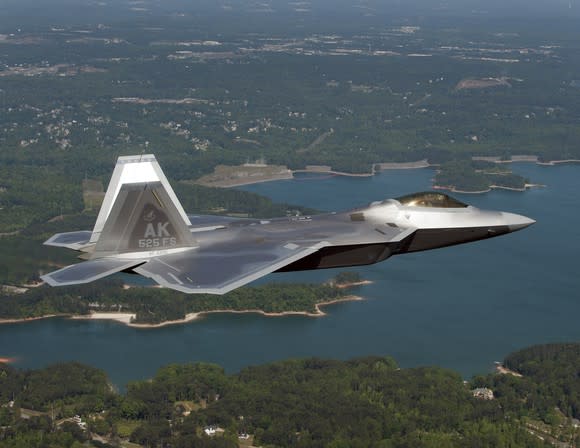 An F-22 Raptor flying over land and water.