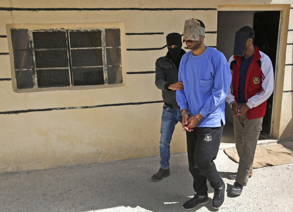 FILE- In this file photo dated Friday, March 30, 2018, a Kurdish security officer escorts Alexanda Kotey, left, and El Shafee Elsheikh, who were allegedly among four British jihadis who made up a brutal Islamic State cell dubbed "The Beatles," at a security center in Kobani, Syria. The Justice Department is preparing to announce charges Wednesday against two men from Britain who joined the Islamic State and were part of a cell that beheaded Western hostages, a law enforcement official said. Their arrival in the U.S. to face charges sets the stage for arguably the most sensational terrorism prosecution since the 2014 case against the suspected ringleader of a deadly attack on the diplomatic compound in Benghazi, Libya. (AP Photo/Hussein Malla)