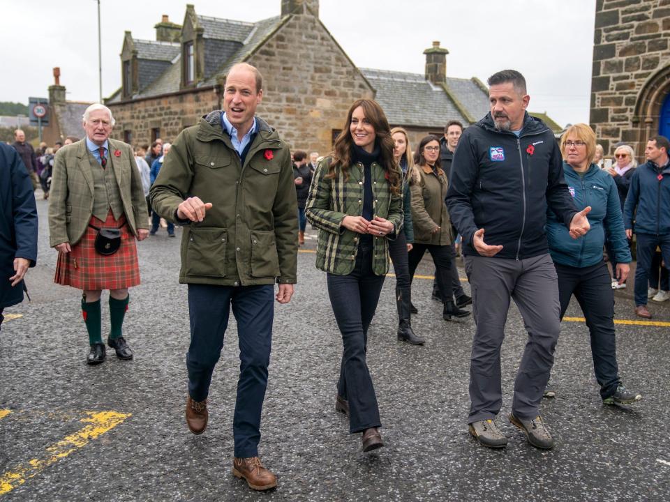 Prince William and Kate Middleton walk through the street with a crowd.