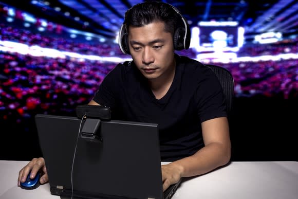 Esports competitive gamer seated in front of laptop in a stadium.