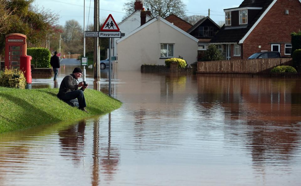 TAUNTON, UNITED KINGDOM - NOVEMBER 25: A man takes a photograph of flood water in the centre of the village of Ruishton, near Taunton, on November 25, 2012 in Somerset, England. Another band of heavy rain and wind continued to bring disruption to many parts of the country today particularly in the south west which was already suffering from flooding earlier in the week. (Photo by Matt Cardy/Getty Images)