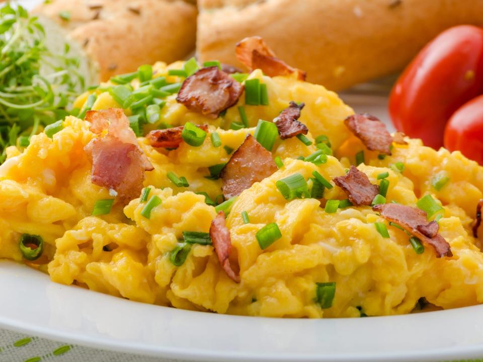 Scrambled eggs with bacon, chive and tomatoes, fresh juice and greens.