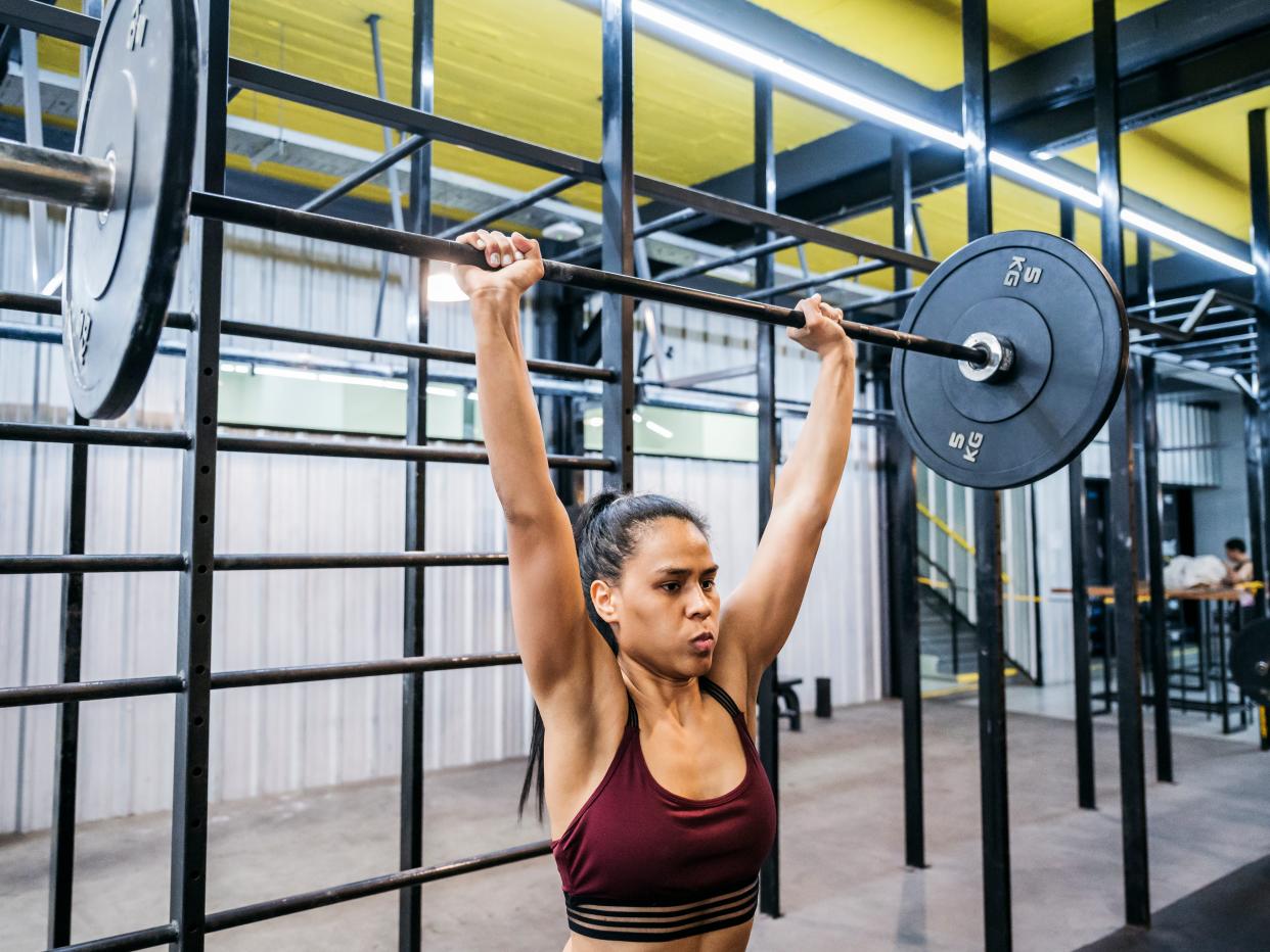 A woman holding a barbell overhead.