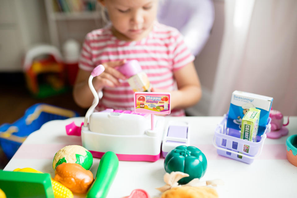 toddler girl playing shops at home with a toy till