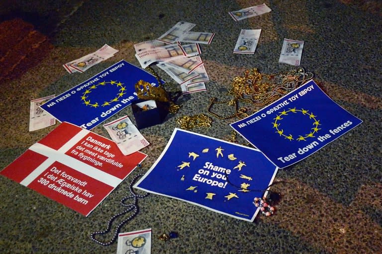 A picture taken on February 2, 2016 shows fake banknotes and some jewelry placed by pro-migrant demonstrators in front of police officers standing guard outside the Danish embassy in Athens, during a protest against Denmark's anti-migrant laws