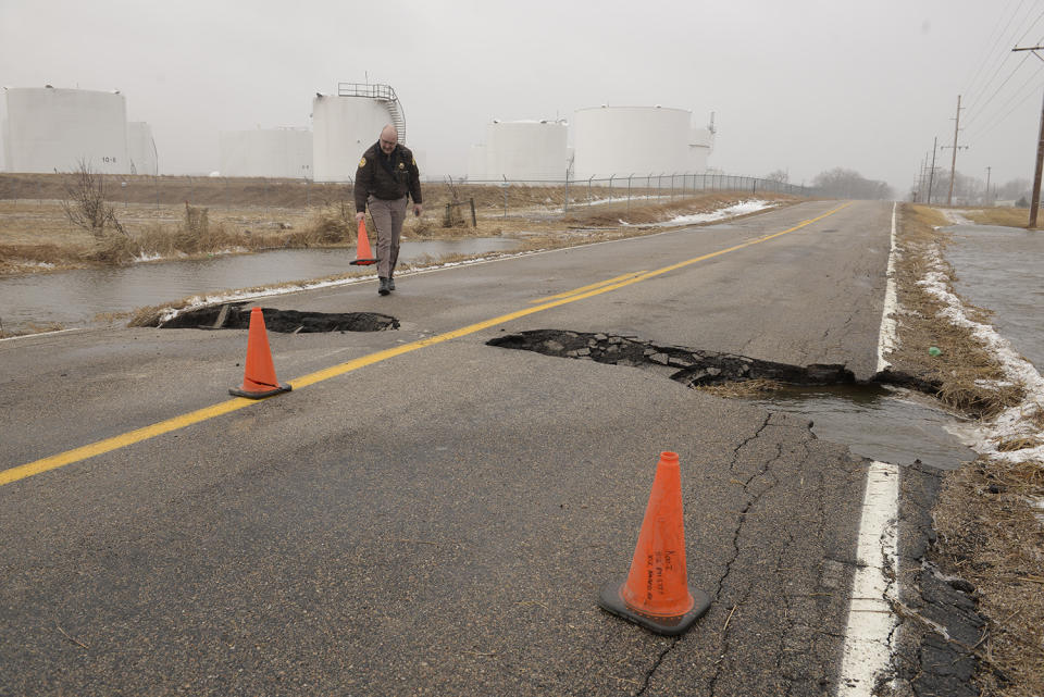 In this March 14, 2019 photo, Madison County Sheriff Todd Volk replaces cones on an area of Kaneb Road north of Norfolk, Neb., that had washed out while making rounds checking on the flooding situation in the county. Thousands of people have been urged to evacuate along eastern Nebraska rivers as a massive late-winter storm has pushed streams and rivers out of their banks throughout the Midwest. (Darin Epperly/The Norfolk Daily News via AP)