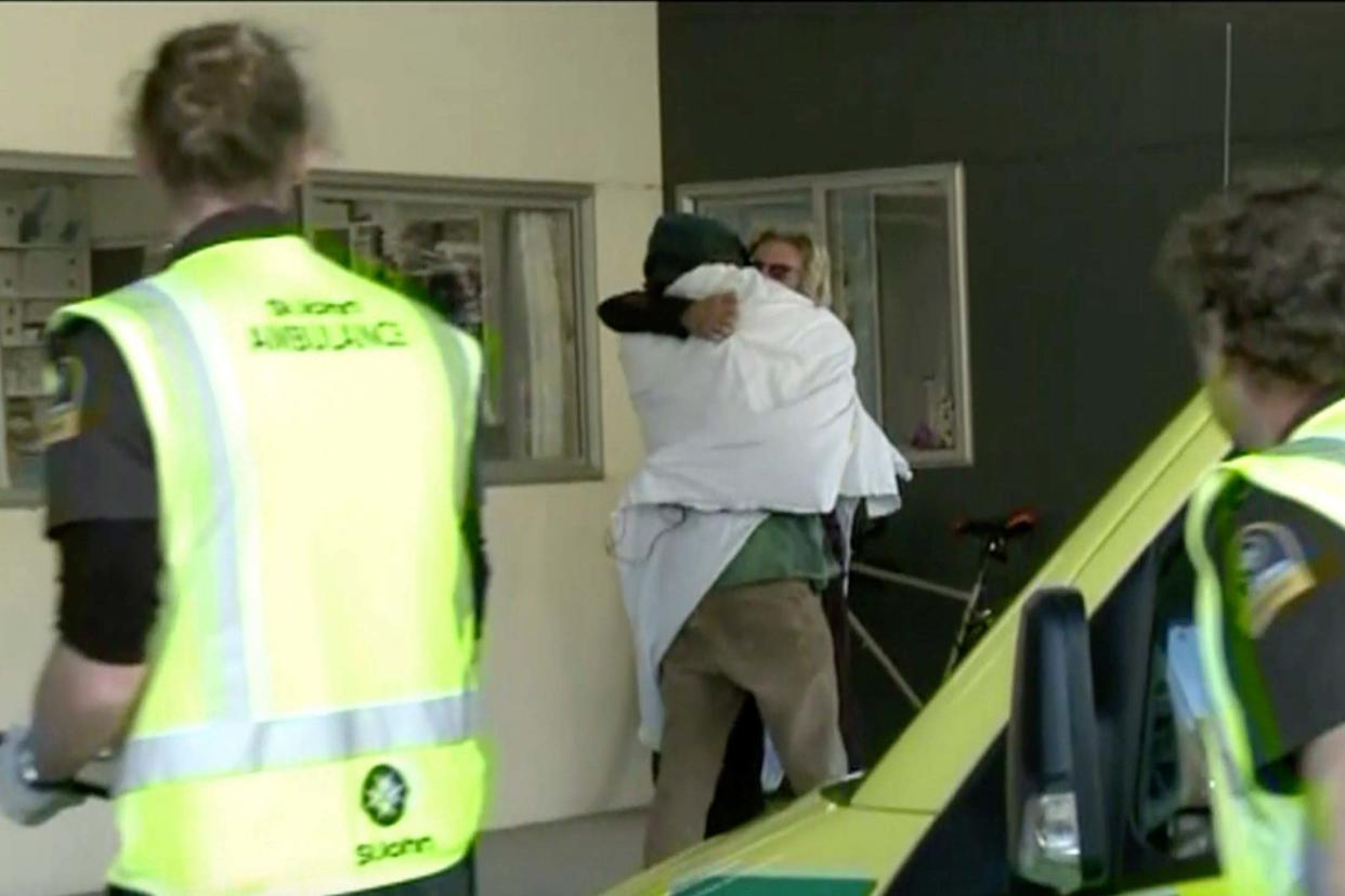 In this image made from May 27, 2020, video, one of the two hikers found alive is wrapped in a white blanket hugs another person as they enter a hospital in Nelson, New Zealand: AP