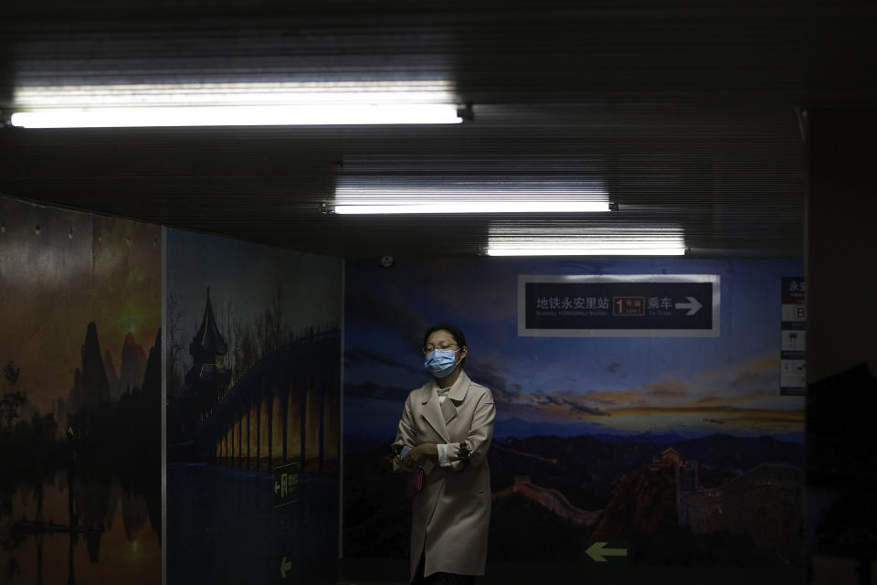 A woman wearing a face mask to help curb the spread of the coronavirus walks by pictures of China's tourism destination on display inside an underpass tunnel in Beijing, Monday, Oct. 19, 2020. (AP Photo/Andy Wong)