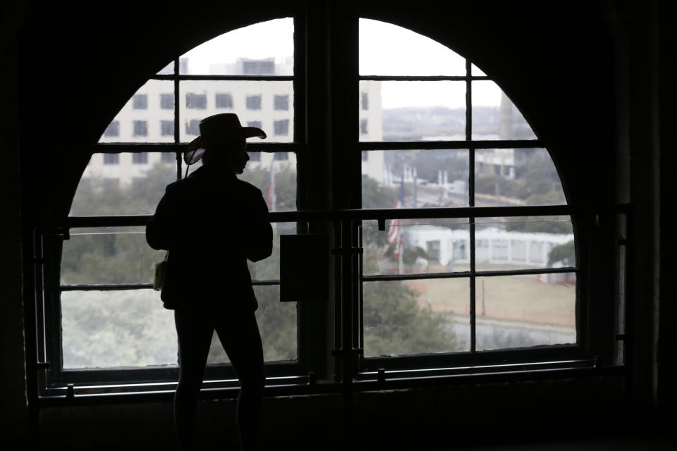 FILE - In this photo made Jan. 25, 2013, a visitor wearing a cowboy hat looks out onto Dealey Plaza from the Sixth Floor Museum located in the former Texas School Book Depository building in Dallas. Three cities loom large in the life and death of John F. Kennedy: Washington, D.C., where he served as U.S. president and as a senator; Dallas, where he died, and Boston, where he was born. With the 50th anniversary of his Nov. 22, 1963 assassination at hand, all three places are worth visiting to learn more about him or to honor his legacy. (AP Photo/LM Otero)