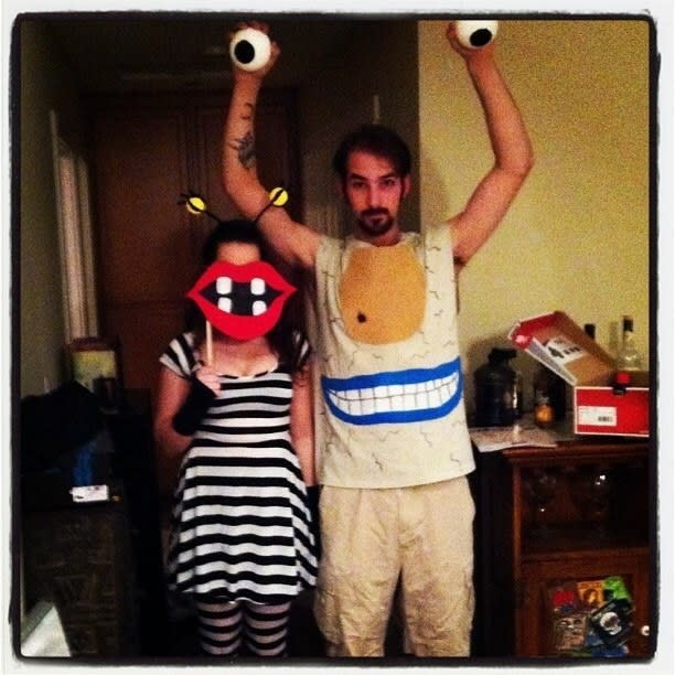 Someone wearing black-and-white stripes while holding a paper cutout of a mouth, and another holding two fake eyeballs over their head