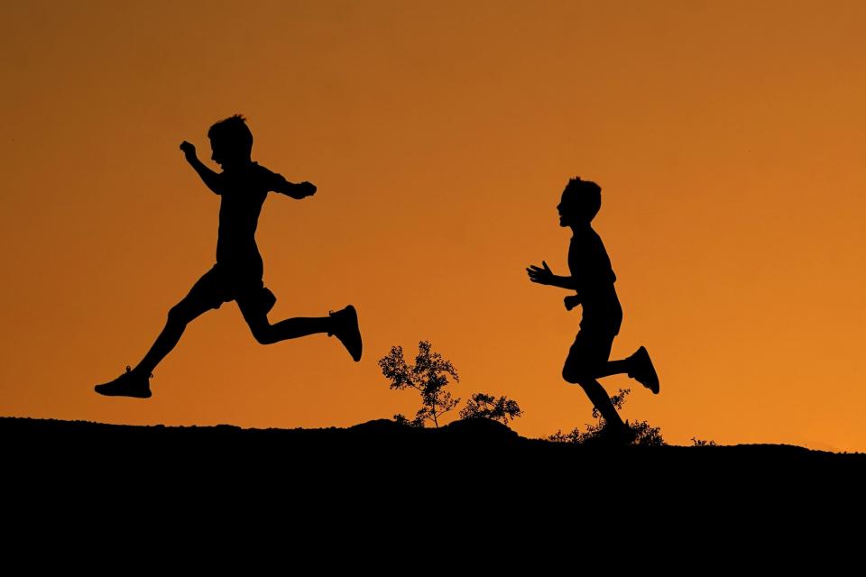 FILE - Boys are silhouetted against the sky at sunset as they run along a ridge at Papago Park, April 1, 2022, in Phoenix. (AP Photo/Charlie Riedel, File)