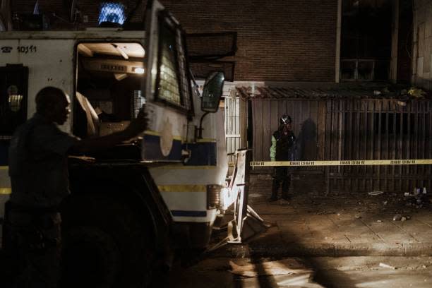 An officer of the South African Police Service (SAPS) climbs on an armoured personnel carrier as a private security guard stands near the entrance of a burned apartment block in Johannesburg on 31 August 2023 (AFP via Getty Images)