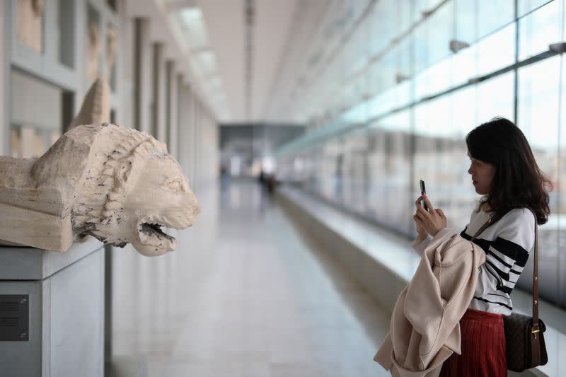 A woman takes a photo as she visits the Parthenon Gallery of the Acropolis Museum, where original sculptures and plaster cast copies of the frieze of the Parthenon temple are exhibited, in Athens