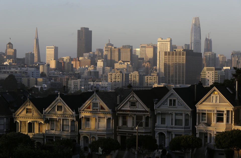 FILE - This July 11, 2017, file photo, shows the skyline beyond a row of Victorian houses in San Francisco. A San Francisco couple has agreed to a $2.25 million legal settlement to the city for illegally renting out 14 apartments as Airbnb units. The San Francisco Chronicle reported Monday, Nov. 5, 2018, that a couple has agreed to pay the sum as penalties and investigation costs. San Francisco requires people renting their homes through sites like Airbnb to live in them at least 275 nights a year and rent them no more than 90 days during that time. (AP Photo/Eric Risberg, File)