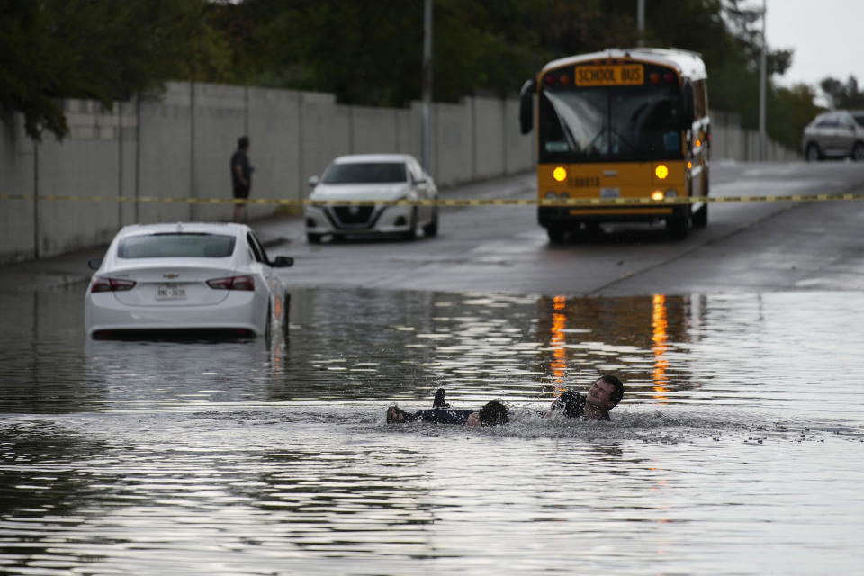 People fall while playing around in floodwaters near a stranded car, Friday, Sept. 1, 2023, in Las Vegas. (AP Photo/John Locher)