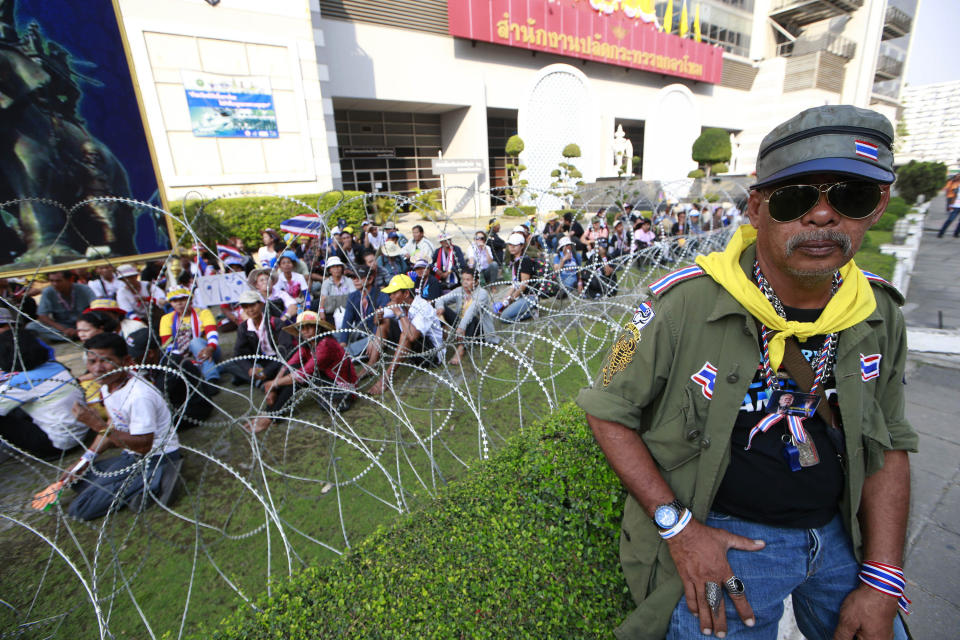 Anti-government protesters sit on the lawn during a rally outside the office of the permanent secretary for defense, background, where Prime Minister Yingluck Shinawatra was reportedly working inside Monday, Feb. 3, 2014 in Bangkok, Thailand. Thai protesters vowed Monday to stage larger rallies in central Bangkok and push ahead their efforts to nullify the results of elections that were expected to prolong a national political crisis. (AP Photo/Wason Wanichakorn)