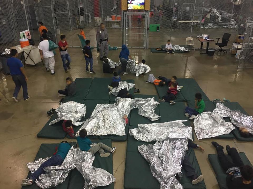 Migrant children sleep in what looks like a fenced-in area. The cage-like structures open up to common areas with portable restrooms, according to the AP.