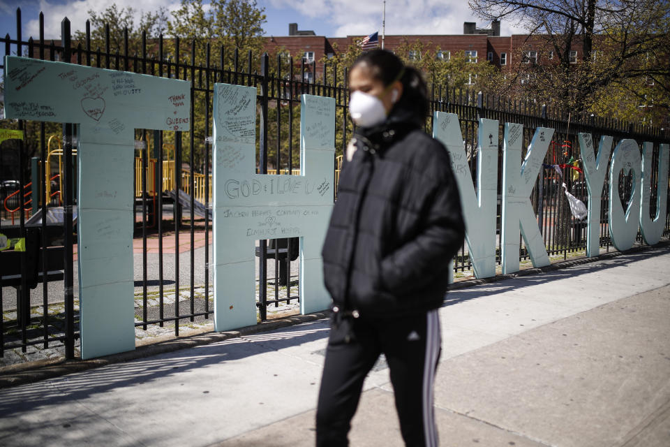 A pedestrian wearing personal protective equipment due to COVID-19 concerns walks past a sign thanking medical personal outside Elmhurst Hospital Center, Thursday, April 16, 2020, in the Queens borough of New York. (AP Photo/John Minchillo)