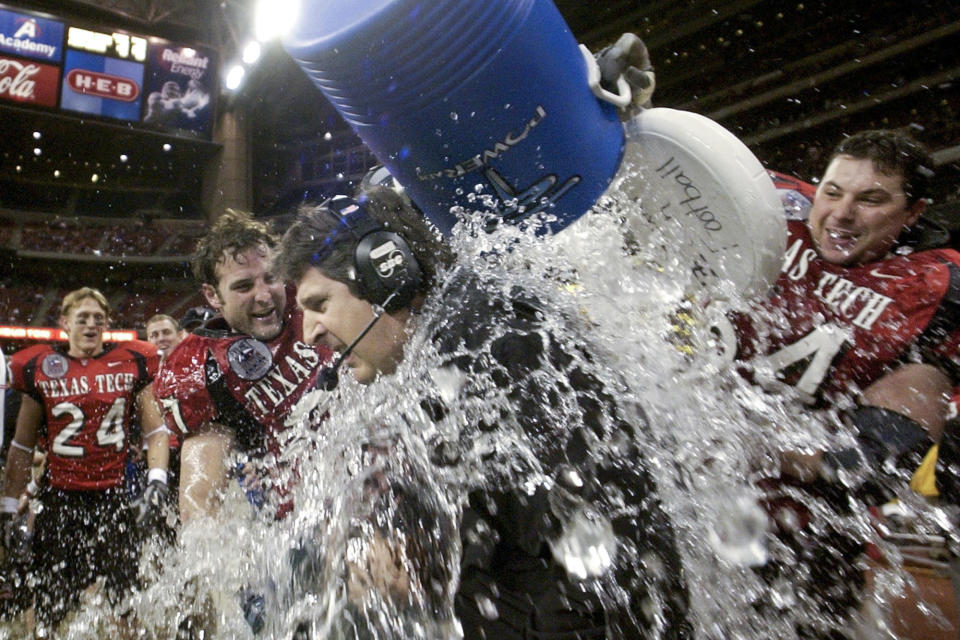 FILE - Texas Tech coach Mike Leach, center, is dunked with water by Wes Welker (27), left, and Cody Campbell (64) right during the final minutes against Navy in the Houston Bowl on Dec. 30, 2003 in Houston. Of the top 25 most-prolific passing seasons in major college football history by yards per game, 12 have direct connections to Hal Mumme and Leach — from Kentucky to Houston to Texas Tech to New Mexico State to Washington State. (AP Photo/David J. Phillip, File)