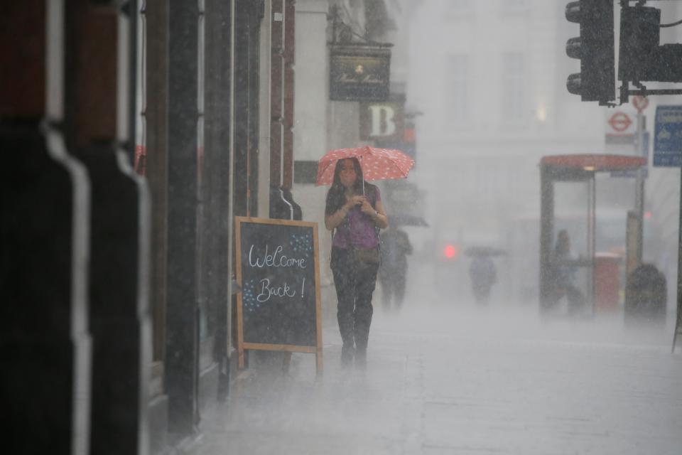 A woman wearing PPE (personal protective equipment), of a face mask or covering as a precautionary measure against COVID-19, shelters under an umbrella they are caught in a downpour of rain on Oxford Street in London on June 17, 2020, as lockdown restrictions imposed to stem the spread of the novel coronavirus continue to be relaxed. - Britain's annual inflation rate slid to 0.5 percent in May, the lowest level in four years, as the country's coronavirus lockdown dampens prices, official data showed Wednesday. (Photo by Tolga AKMEN / AFP) (Photo by TOLGA AKMEN/AFP via Getty Images)