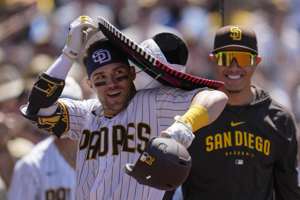 San Diego Padres' Brett Sullivan, left struggles with a sombrero after hitting a two-run home run as teammate Manny Machado looks on, right, during the fourth inning of a baseball game against the Cincinnati Reds, Wednesday, May 3, 2023, in San Diego. (AP Photo/Gregory Bull)